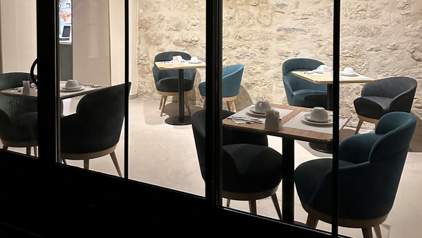 A dining area with tables and chairs, a stone wall, and a view through large windows. - Hôtel Médieval (Avignon)
