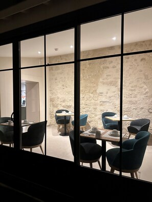 Un comedor con mesas y sillas, un muro de piedra y vistas amplias a través de grandes ventanales.