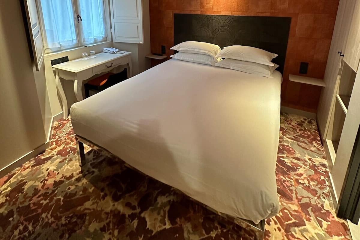 A hotel room with a bed, a desk, and a window with curtains.