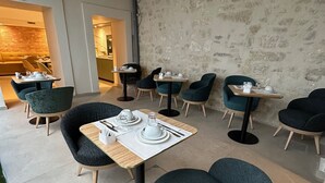 A modern dining area with round tables and chairs, a stone wall, and a wooden ceiling. - Hôtel Médieval (Avignon)