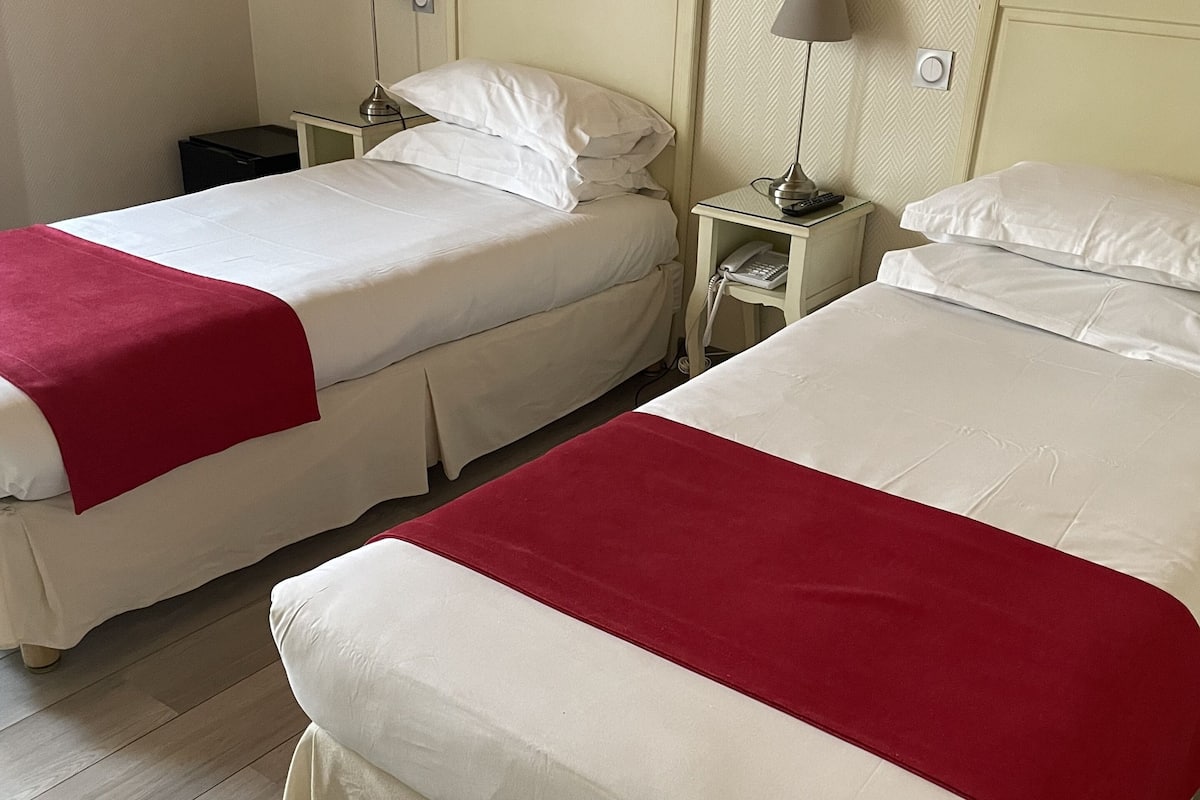 Two single beds with white linens and red bedspreads, a nightstand with a lamp and phone, and a wall-mounted painting.