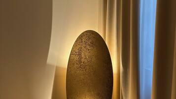 A corner room with a textured spherical floor lamp on a carpeted floor, beige curtains, and a plain wall.