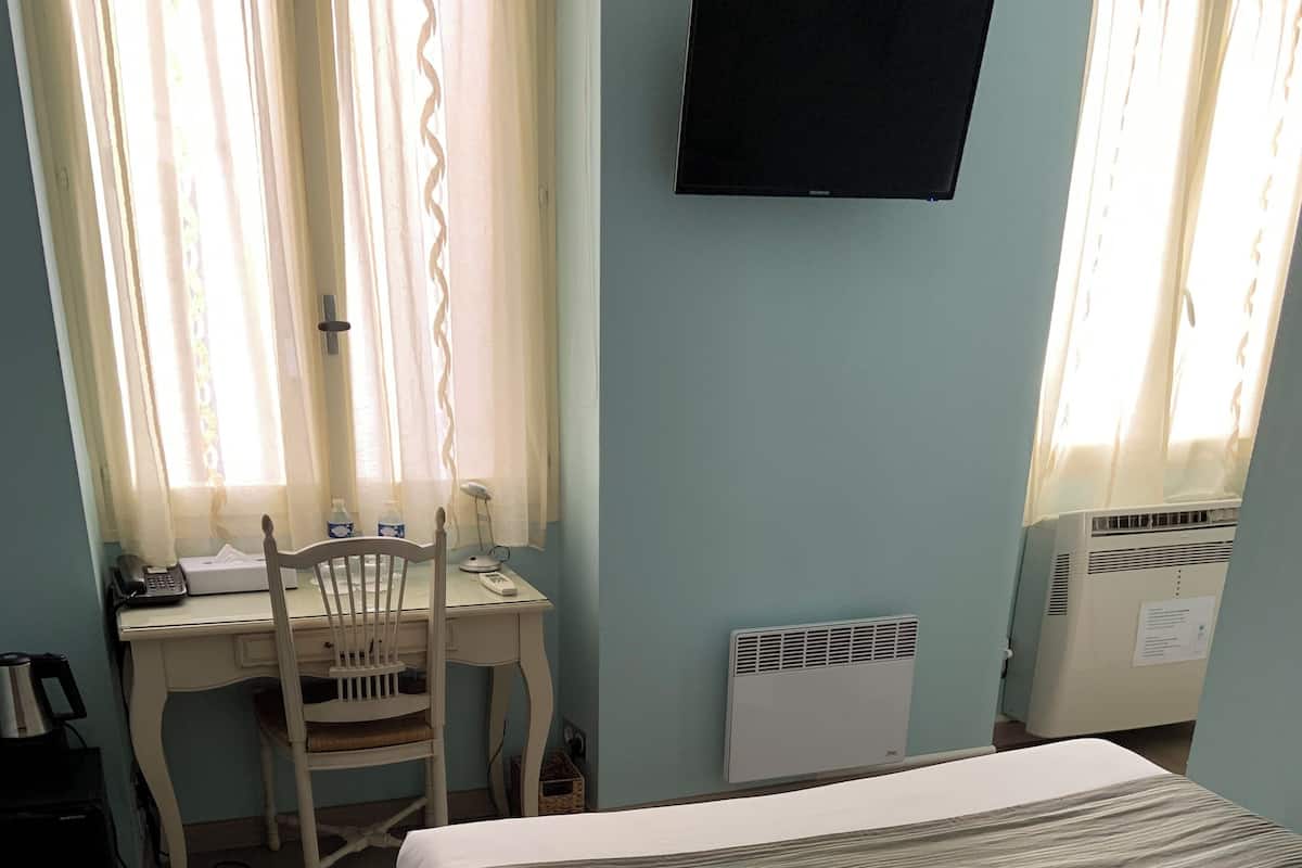 A bedroom with a bed, a desk with a chair, a television, and a radiator.