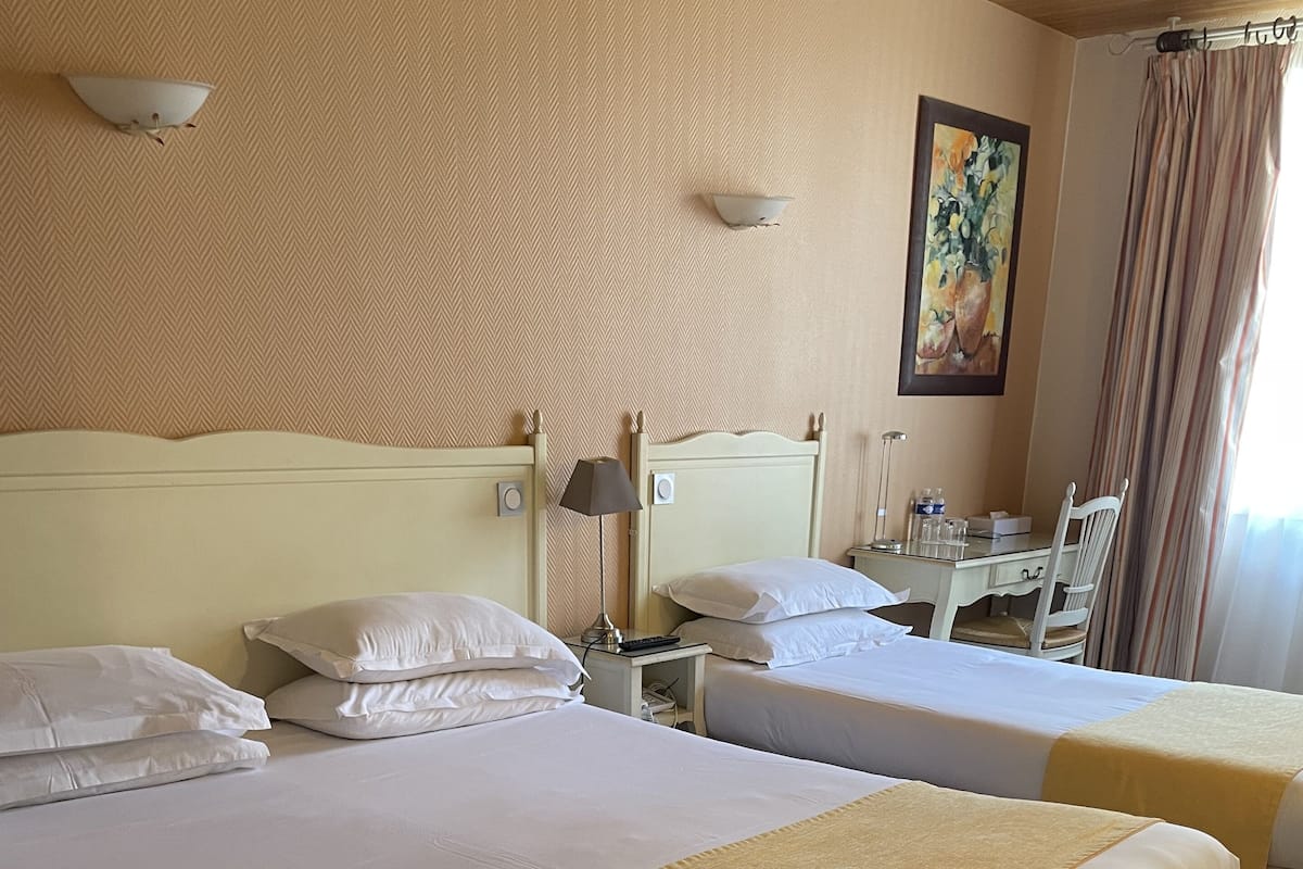 A hotel room with two beds, a desk, and a chair.