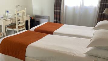 A hotel room with two beds, a desk, a chair, a TV, and a window with curtains.