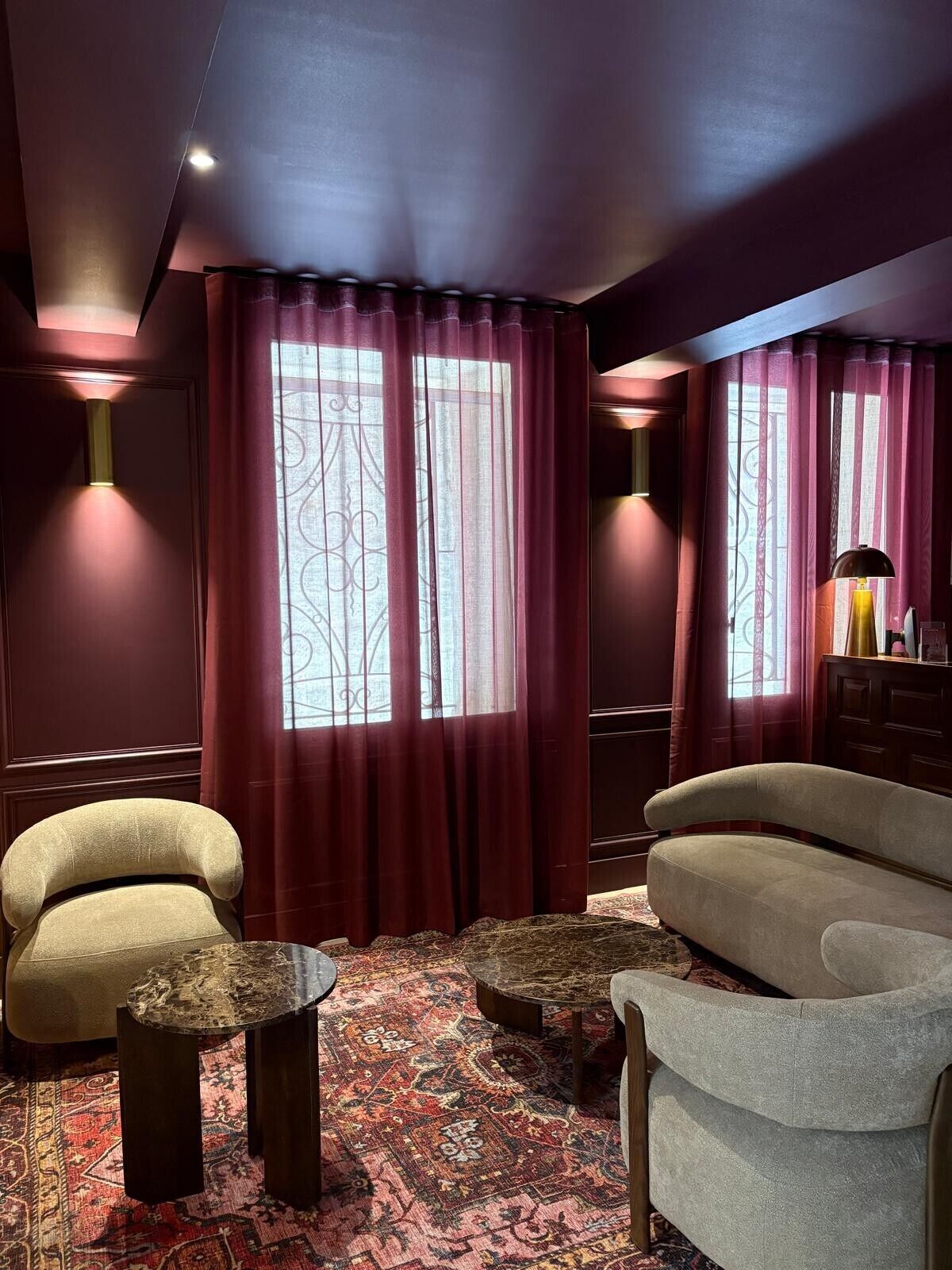 A room with a sofa, two armchairs, a patterned rug, and a decorative window with curtains.