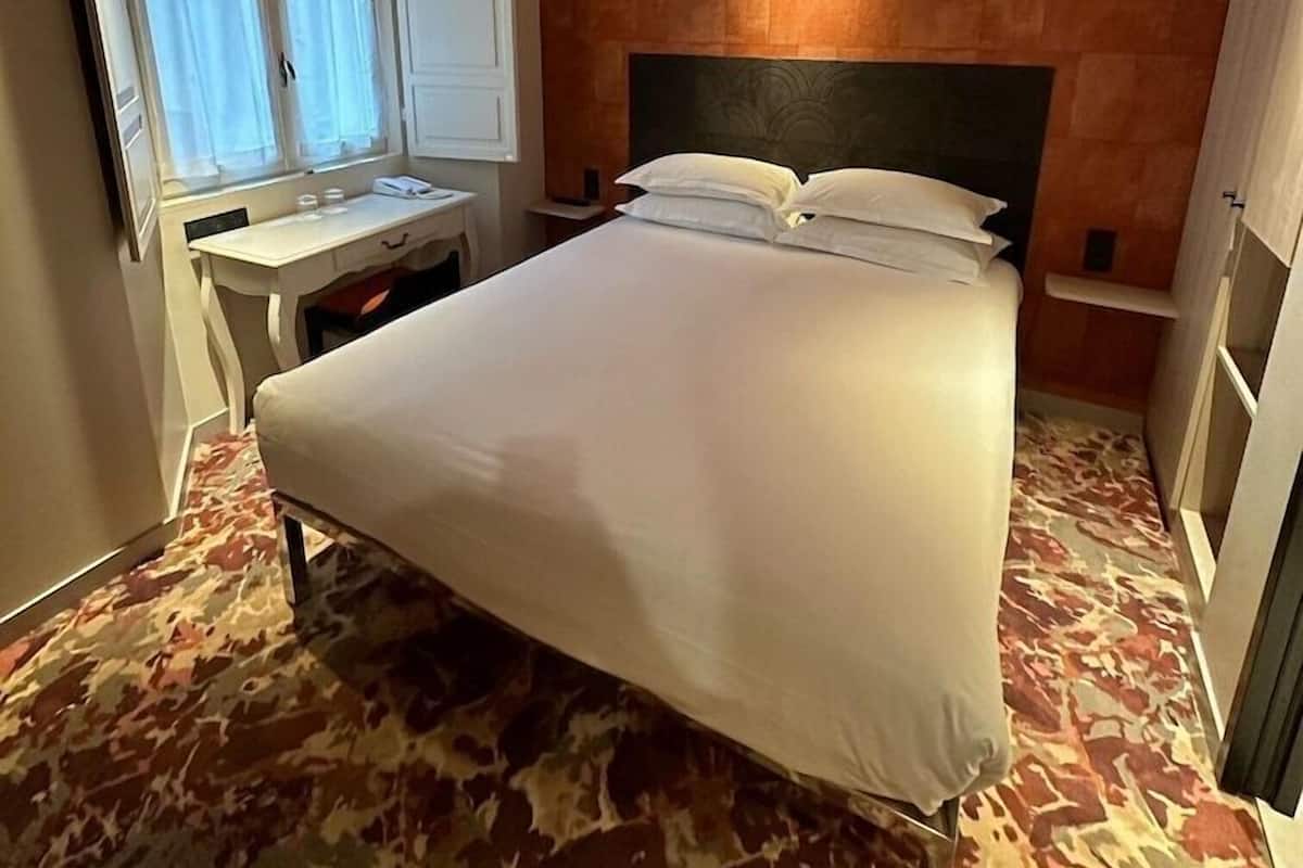 A hotel room with a bed, a desk, a mirror, and a window with curtains.