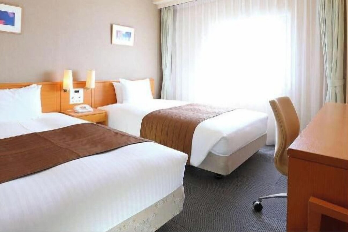A hotel room with two beds, a desk, and a chair.