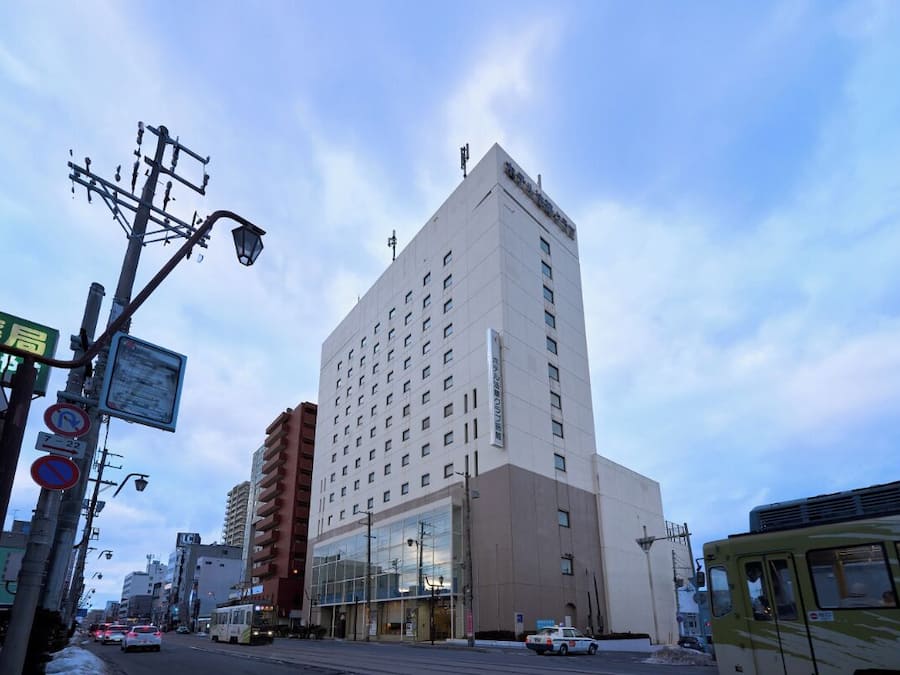 Um hotel de vários andares com fachada moderna, situado numa rua urbana movimentada, com trânsito visível e um elétrico.