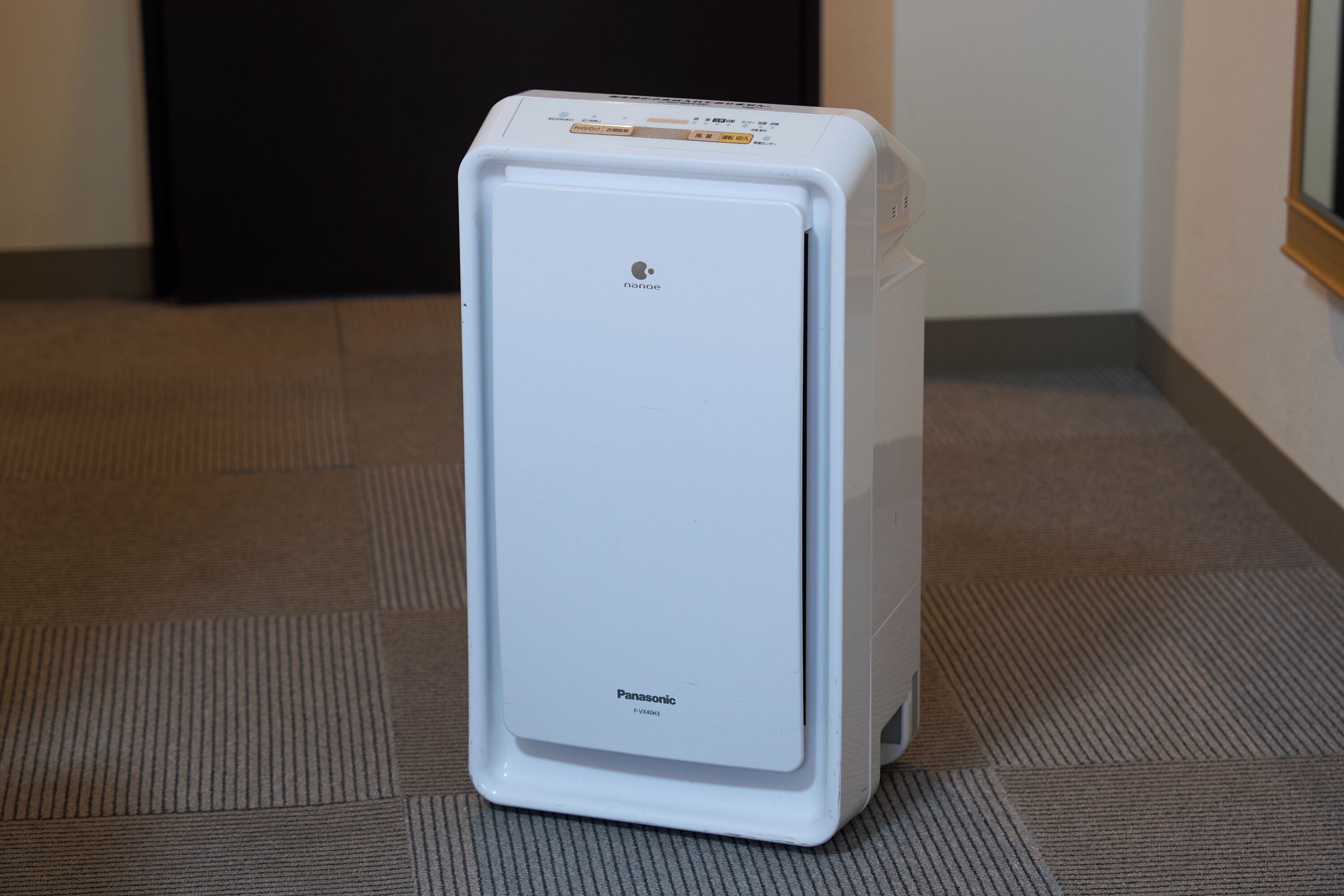 A white Panasonic F-VX40H3 refrigerator in a room with a patterned carpet and a plain wall.