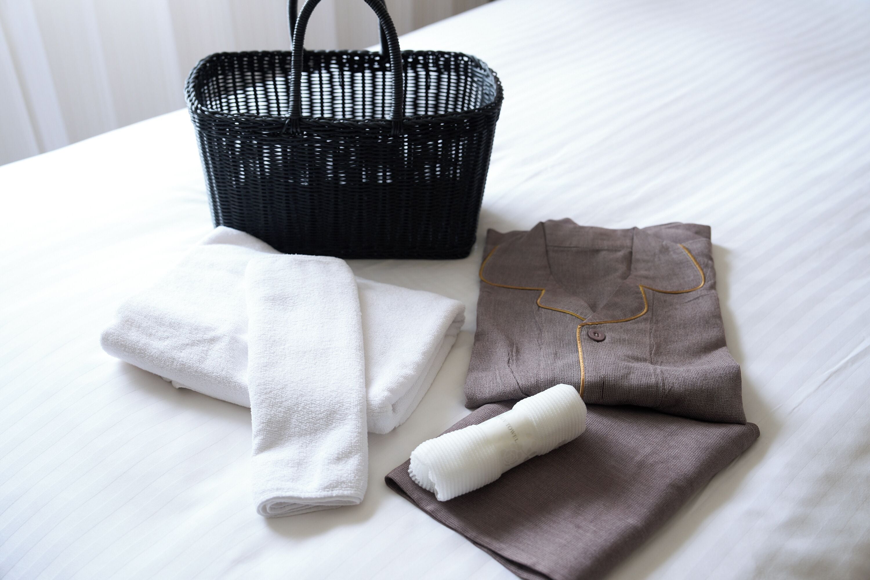 A neatly made bed with a black woven basket and folded towels.