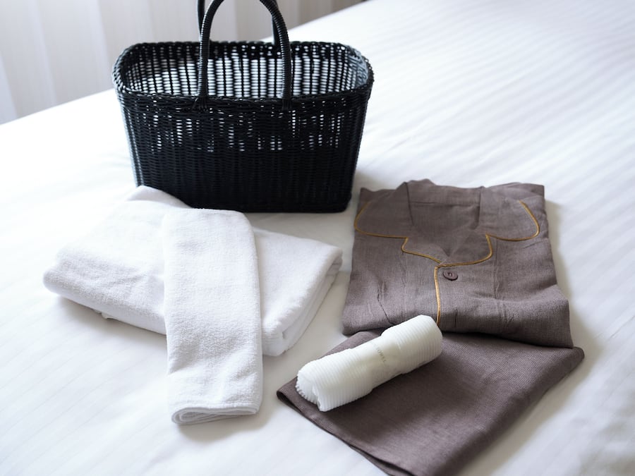 A neatly made bed with a black woven basket and folded towels.