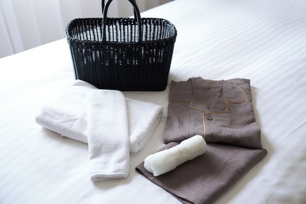 Una cama bien hecha con una cesta negra trenzada y toallas dobladas.