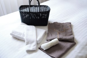 Una cama bien hecha con una cesta negra trenzada y toallas dobladas.