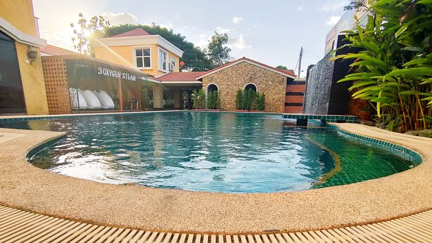 Una piscina con borde de piedras, un edificio de piedra con techo rojo y un letrero que dice '30XVGEN STEAM'.