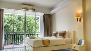 Habitación de hotel con una cama grande, una mesita de noche, una lámpara de pared y vistas a la vegetación a través de la ventana.