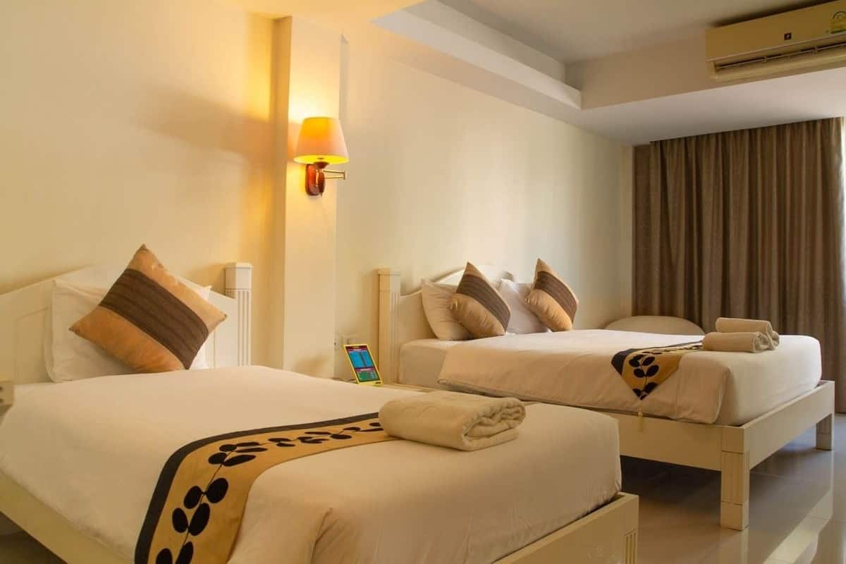 Ein Hotelzimmer mit zwei Betten, jeweils mit Kopfkissen und Decke. An der Wand befindet sich eine Lampe, darüber eine Klimaanlage.