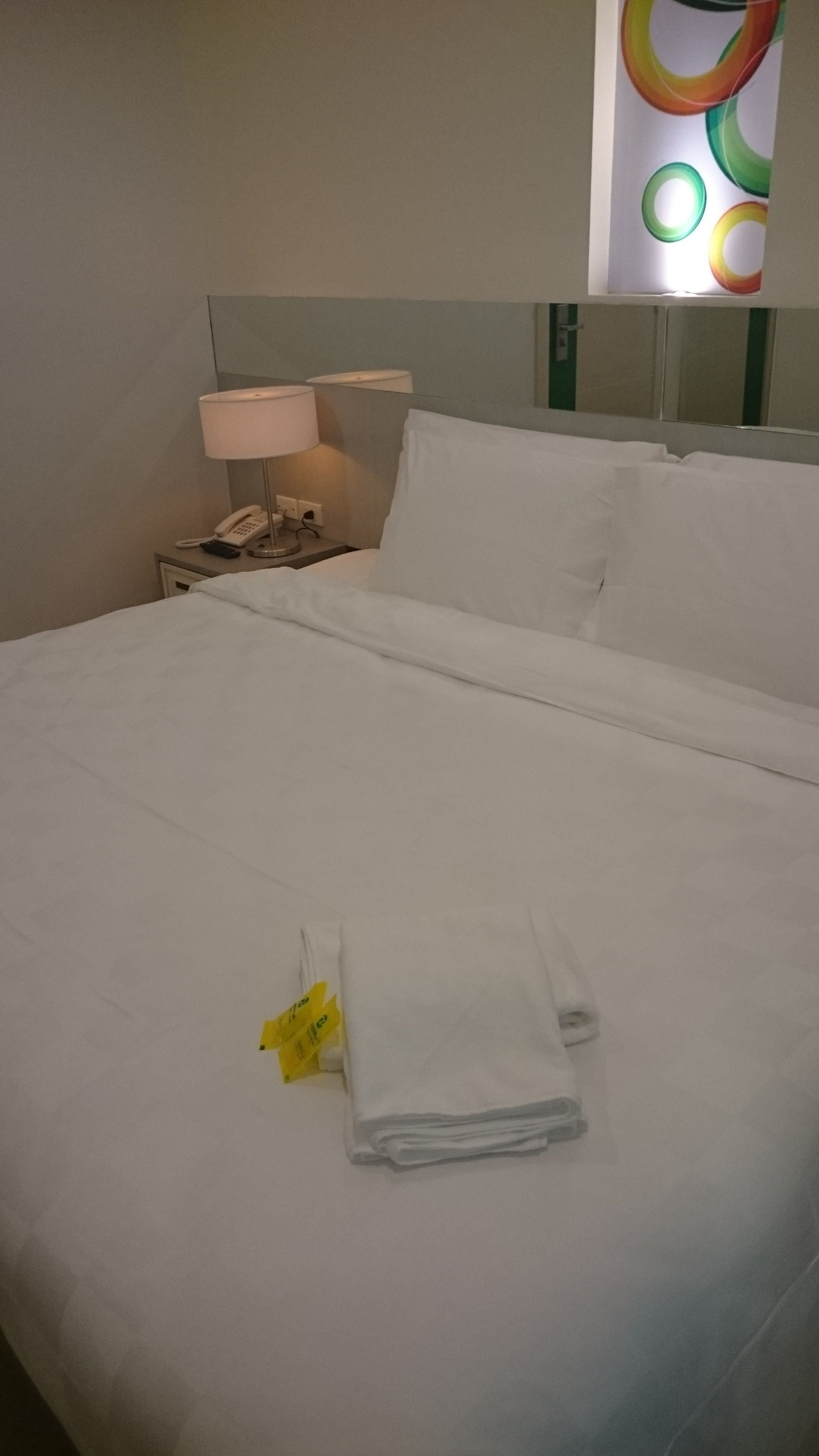 A neatly made bed with white linens, a folded towel, and a yellow towel on the bed.