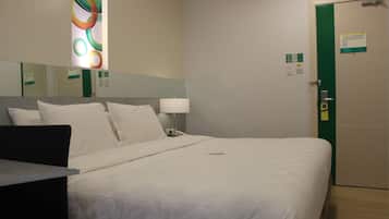 Comfortable accommodations feature a neatly made bed, bedside table, and lamp, along with a large mirror and convenient room amenities.