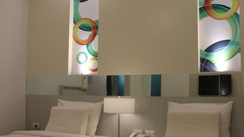 A hotel room with two beds, a bedside table with a lamp, and a wall-mounted TV.