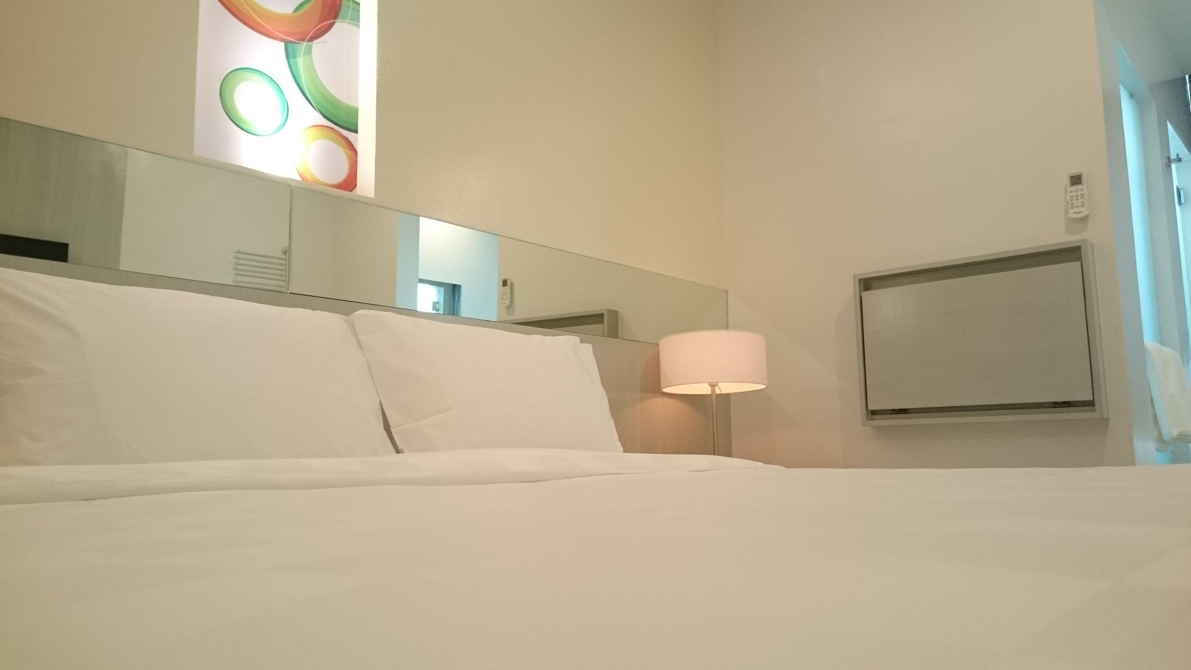 Une chambre d’hôtel avec un lit, une lampe, une télévision et un miroir.