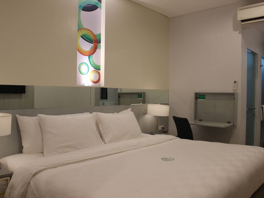 Una habitación de hotel con una cama grande, dos lámparas de noche, un espejo y una pequeña estantería.