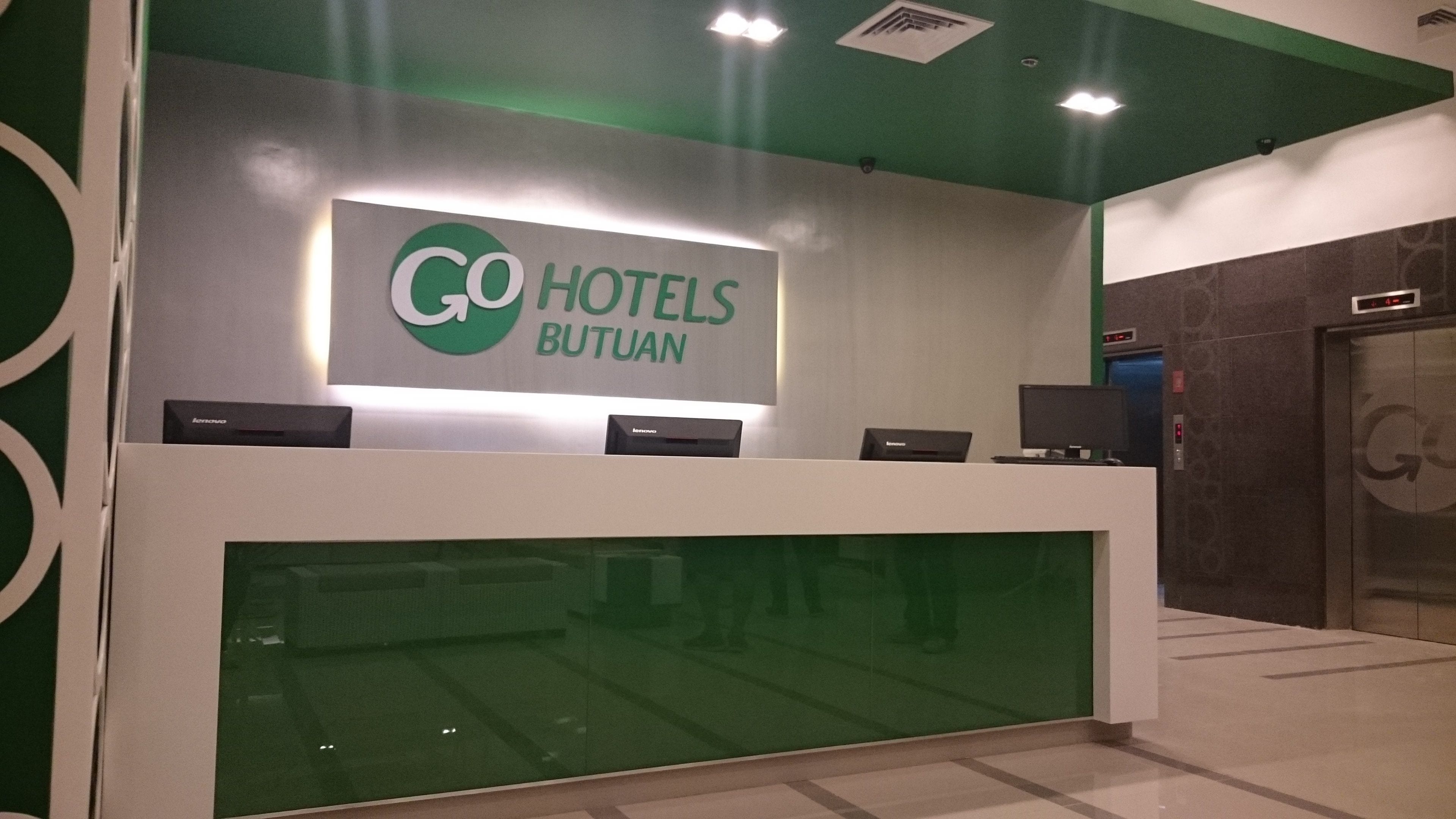A reception desk with a sign reading "GO HOTELS BUTUAN" and a digital clock displaying 4:30.