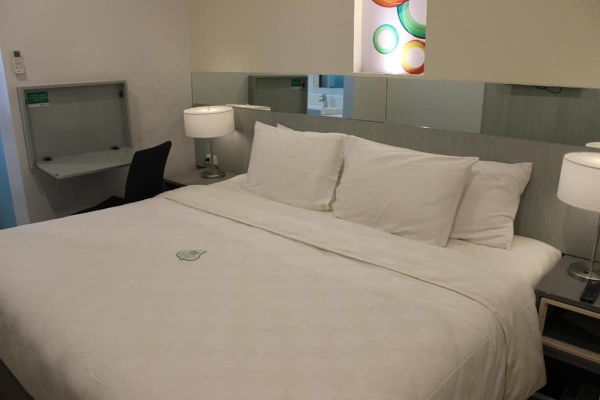 A hotel room with a bed, bedside tables, a desk, and a mirror.