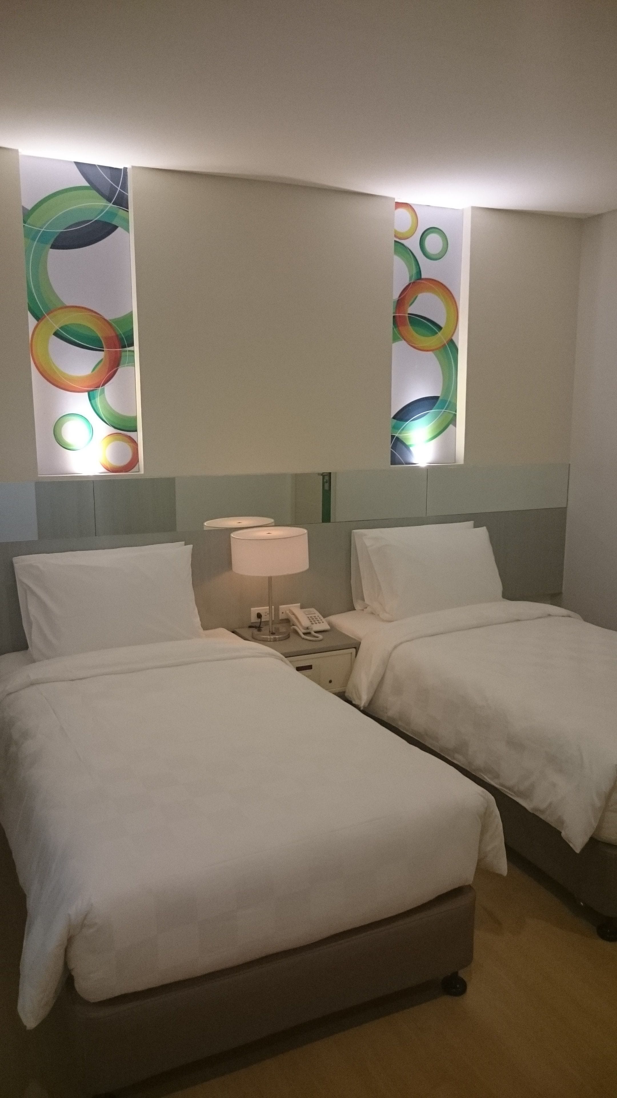 A hotel room with two beds, a nightstand with a lamp and phone, and a wall with abstract art.