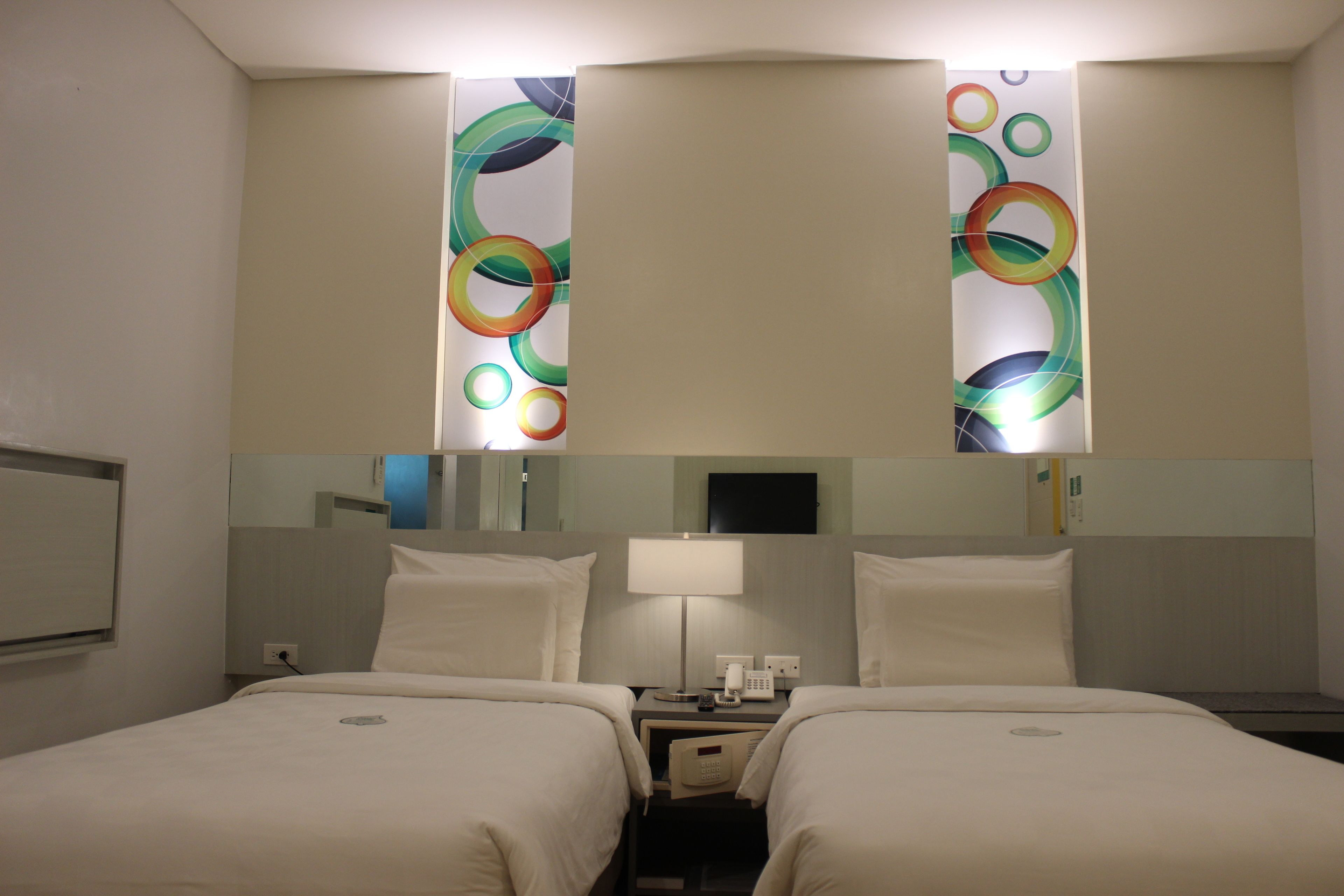 A hotel room with two beds, a nightstand, a lamp, and a mirror.