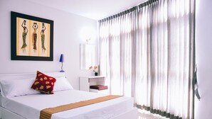 A hotel room with a large bed, a nightstand, a mirror, and a window with sheer curtains. - Golden On-nut (Bangkok)