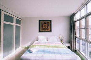 A hotel room with a bed, a window with curtains, a wall-mounted artwork, and a view of the outside.