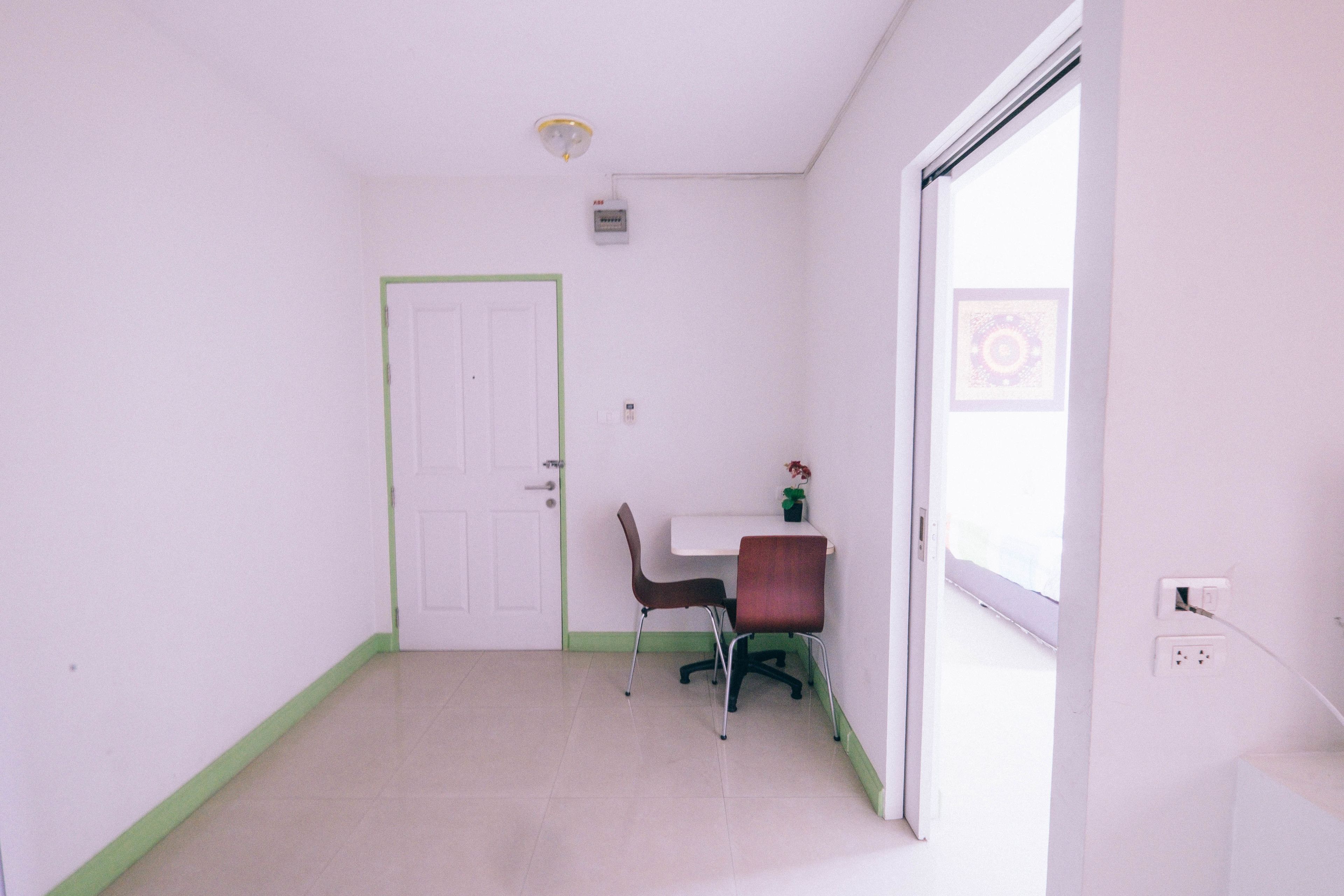 A small, clean room with a white door, a small table with a chair, and a window with a view of a building.