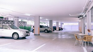A parking garage with multiple cars parked, concrete pillars, and a table with chairs. - Golden On-nut (Bangkok)