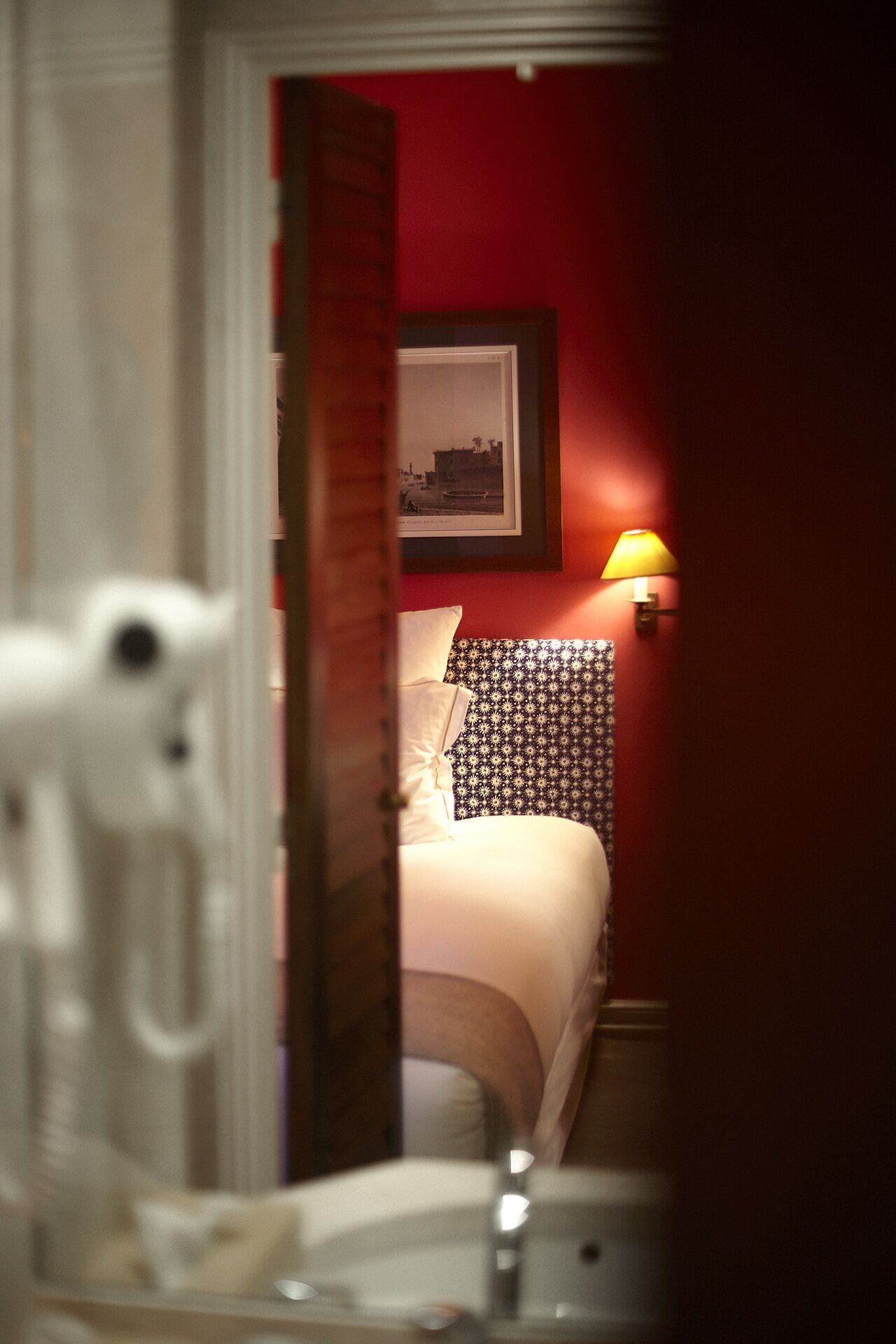 A hotel room with a bed, a pillow, a wall-mounted picture, and a bedside lamp.