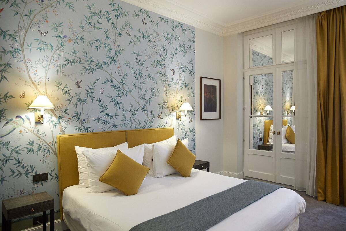 A hotel room with a bed, two bedside lamps, a framed picture on the wall, and a window with curtains.
