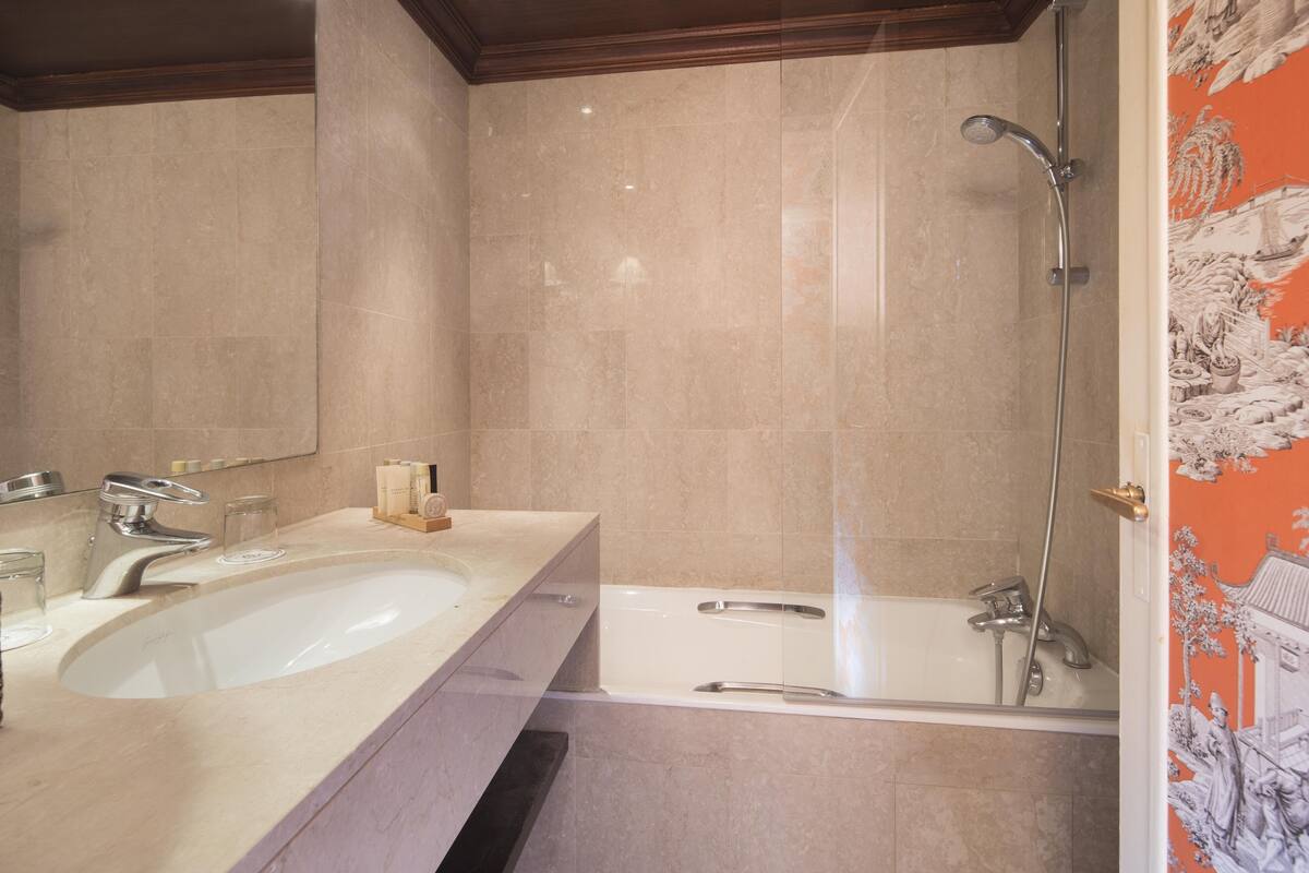 A bathroom with a sink, mirror, shower, and a decorative wall.