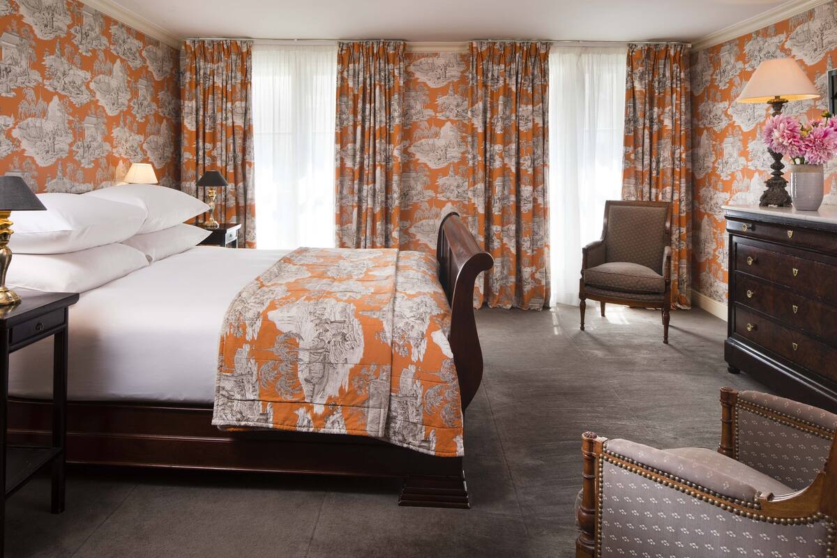 A hotel room with a large bed, a wooden chair, a dresser, and curtains with a floral pattern.