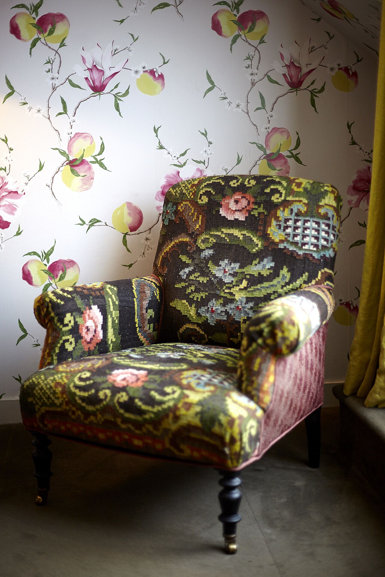 Ein Stuhl mit floralem Bezug vor einer Tapete mit Frucht- und Blumenmotiven.
