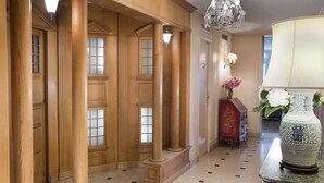 A grand hallway with wooden columns, a chandelier, and a vase with flowers on a table. - Hotel du Danube Saint Germain (Paris)