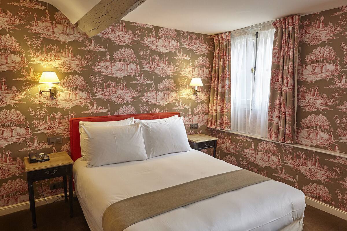 A hotel room with a large bed, two bedside tables, a nightstand, and floral wallpaper.