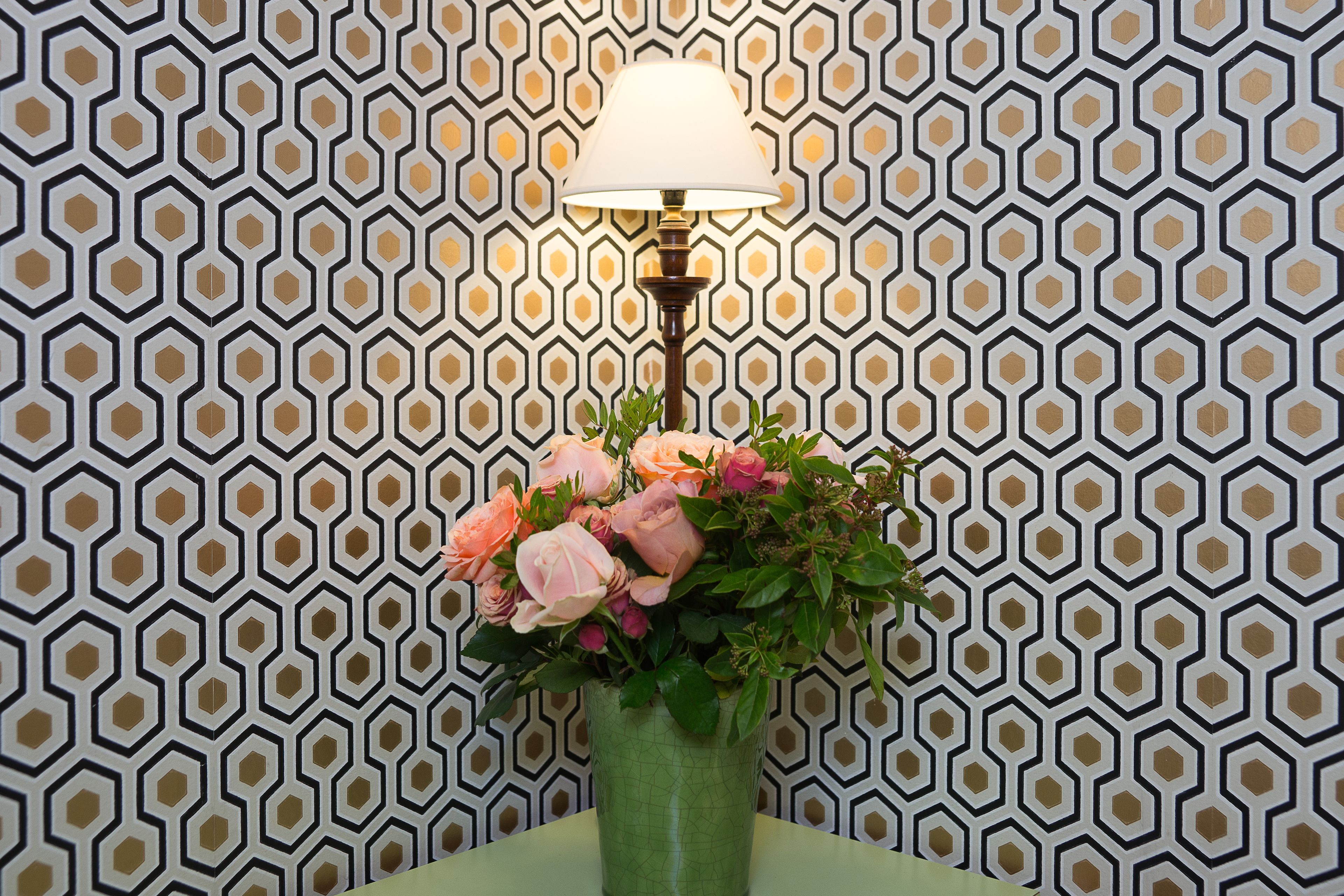 A green vase with pink flowers on a table against a patterned wall.