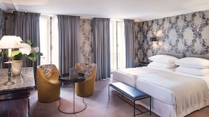 A hotel room with a large bed, a desk with a lamp, two chairs, and a small table. - Hotel du Danube Saint Germain (Paris)