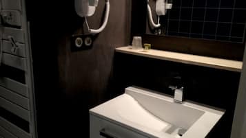 Een badkamer met een witte wasbak, een spiegel en een haardroger bevestigd aan de muur.