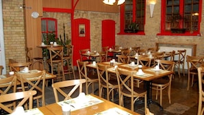 Un restaurante con mesas y sillas de madera, detalles en rojo y paredes de ladrillo.
