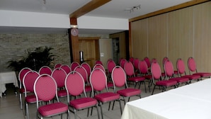 Un salón de conferencias con filas de sillas rosas y una larga mesa, una pared de ladrillo y una puerta de madera.