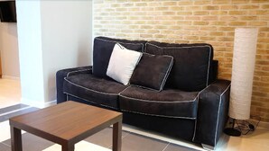 Un sofá de cuero negro con detalles blancos, una mesa de centro de madera y una pared de ladrillo.