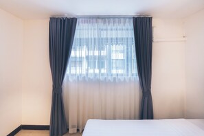 A hotel room with a bed, a window with curtains, and a wall-mounted air conditioning unit. - Atlas Bangkok Hotel (Bangkok)