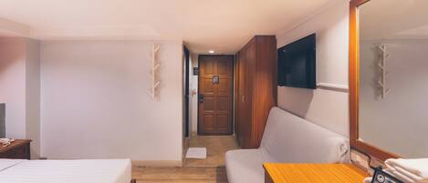 A hotel room with a bed, a sofa, a wooden table, a TV, and a door leading to another room.