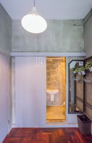 A compact bathroom with a visible sink, a hanging light fixture, and a door leading to a shower area. - Atlas Bangkok Hotel (Bangkok)